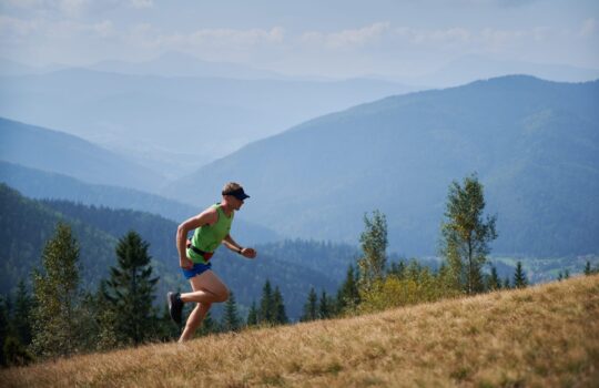 Athletic young man running up the hill in mountains.